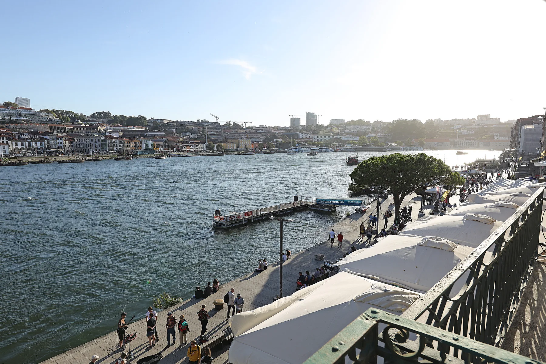 A riverside promenade with outdoor seating and buildings across the water.