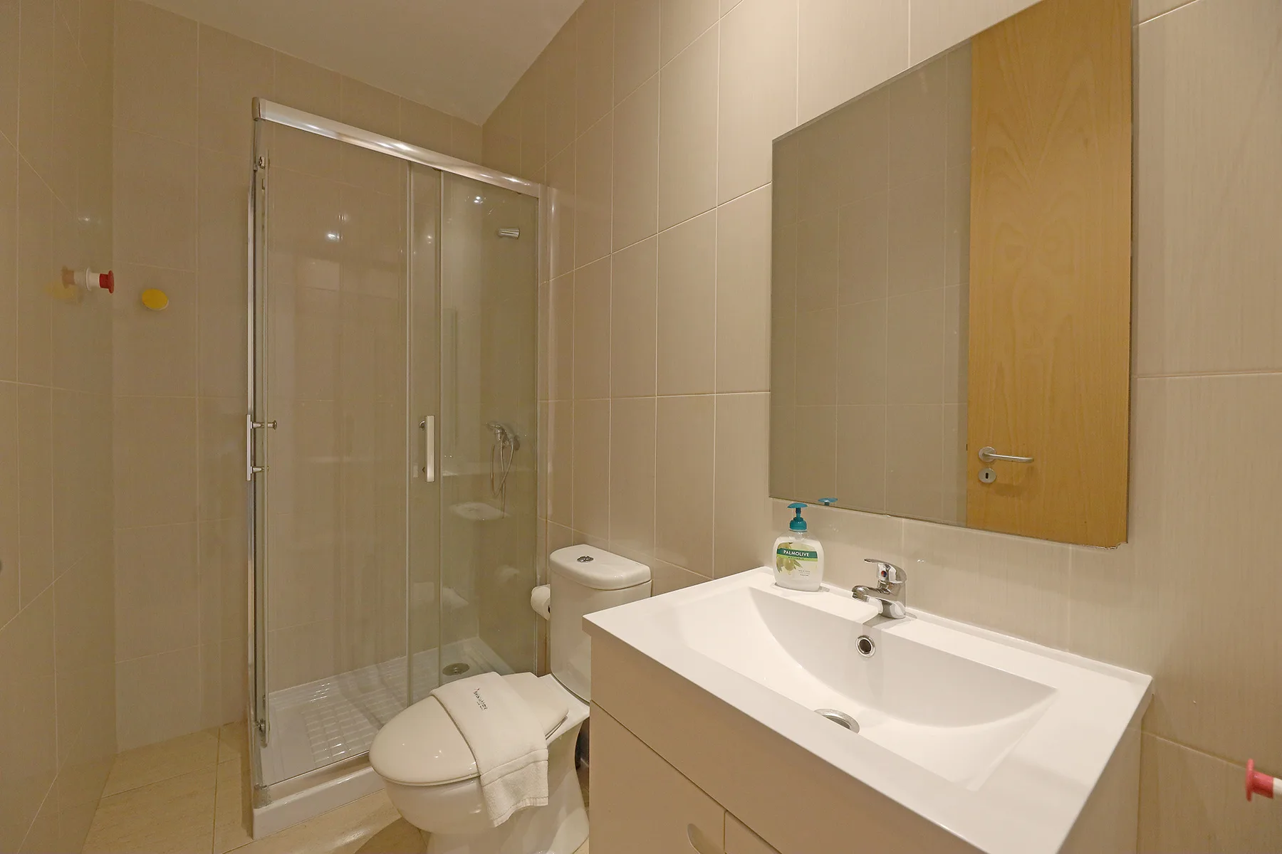 A tiled bathroom with a shower, toilet, and sink beneath a wall mirror.
