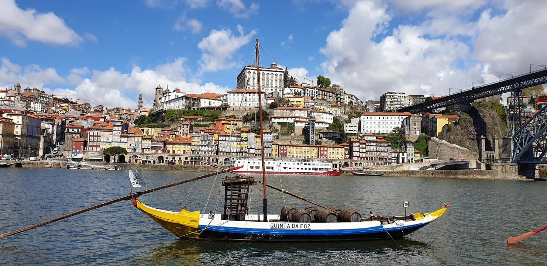 A colorful riverside cityscape with a traditional boat on the water.