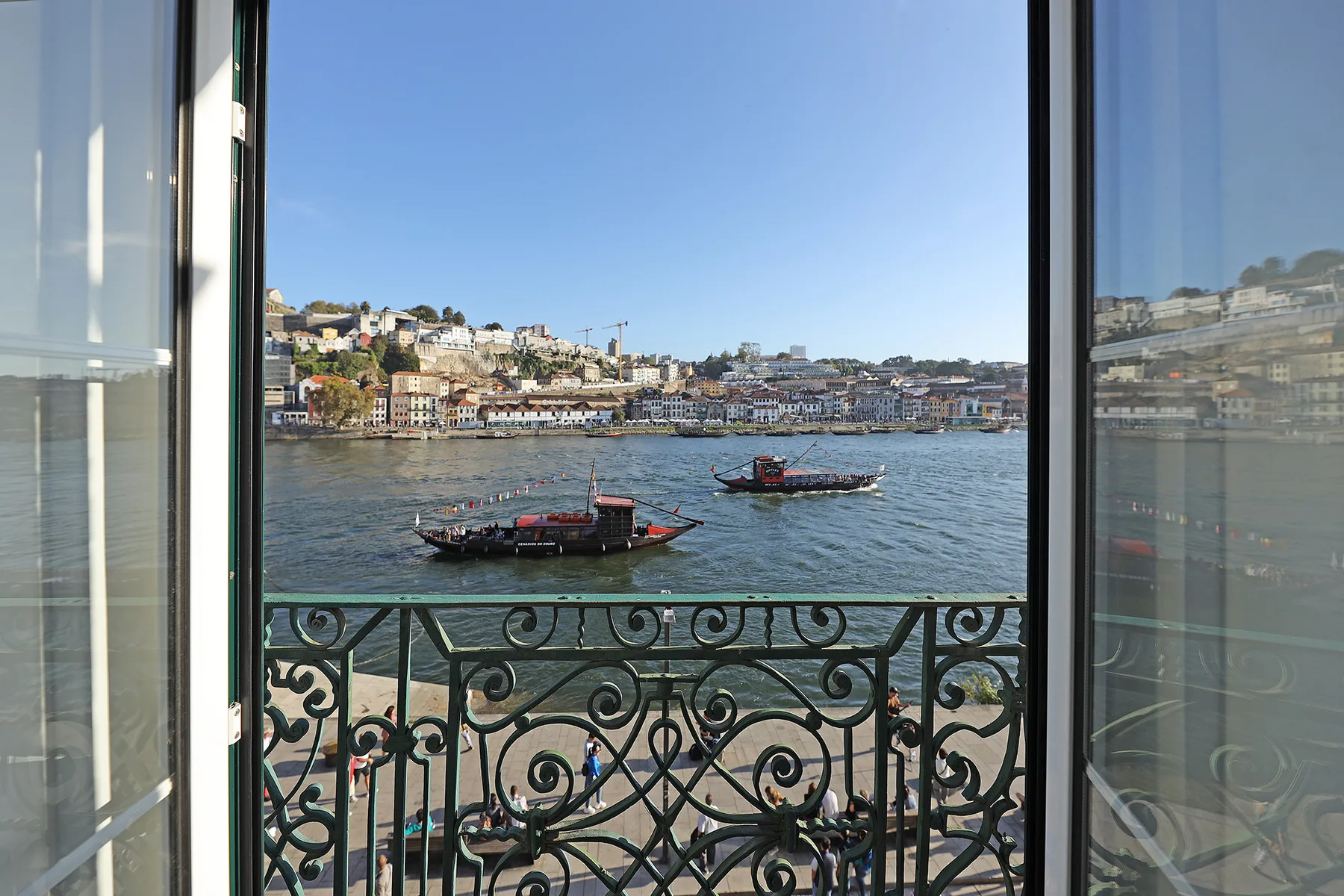 A river view through open glass doors, with boats and hillside buildings beyond the railing.