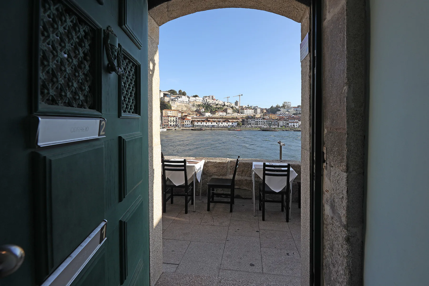 An open doorway frames a riverside terrace with seating and a view across the water.