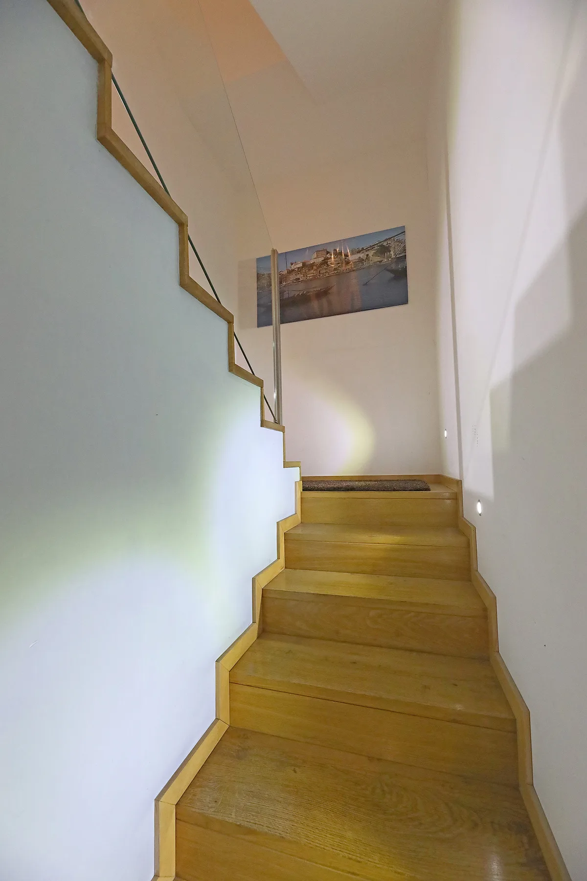 A wooden staircase rises beside white walls, with a framed cityscape at the top.