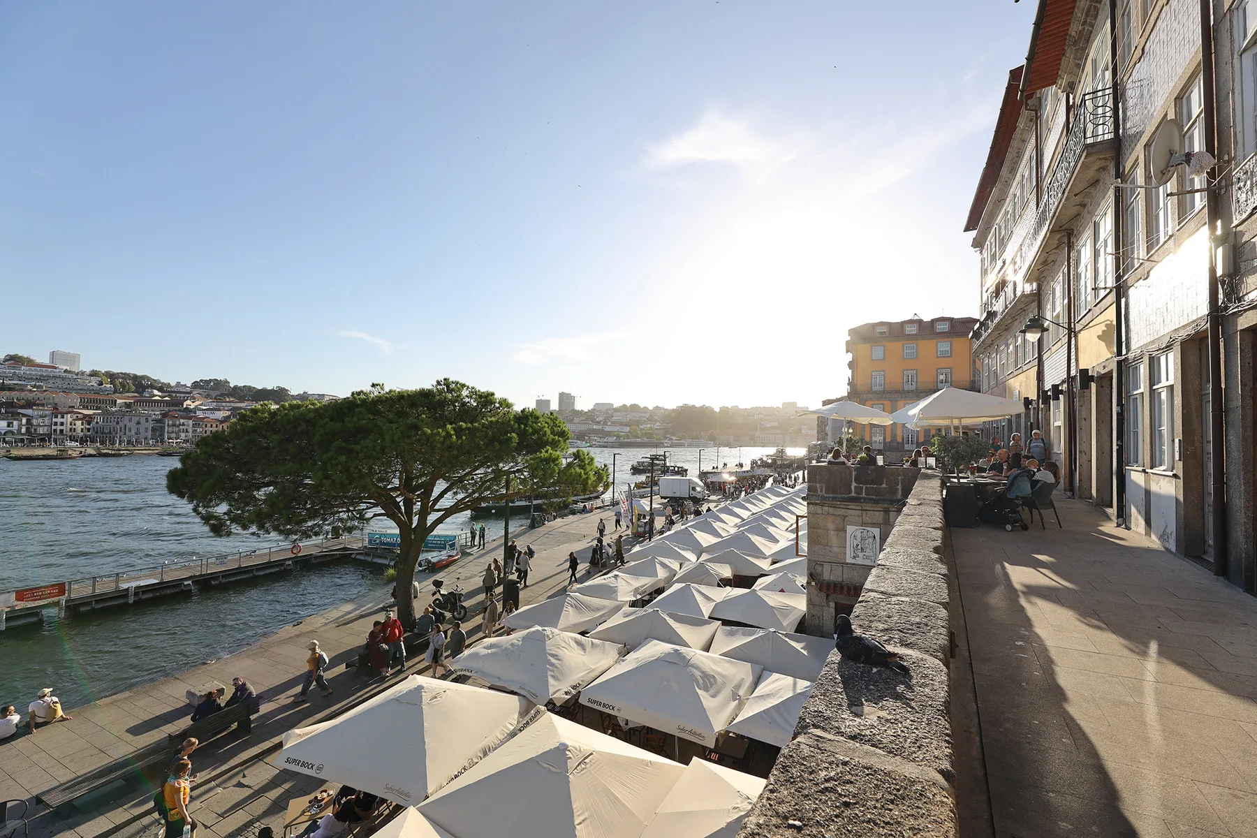 Riverside promenade with outdoor café seating and a view across the water.