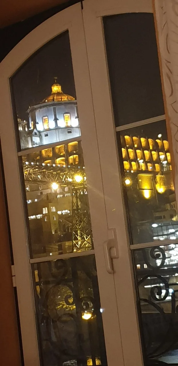 A nighttime city view through a window, with a brightly lit historic building.