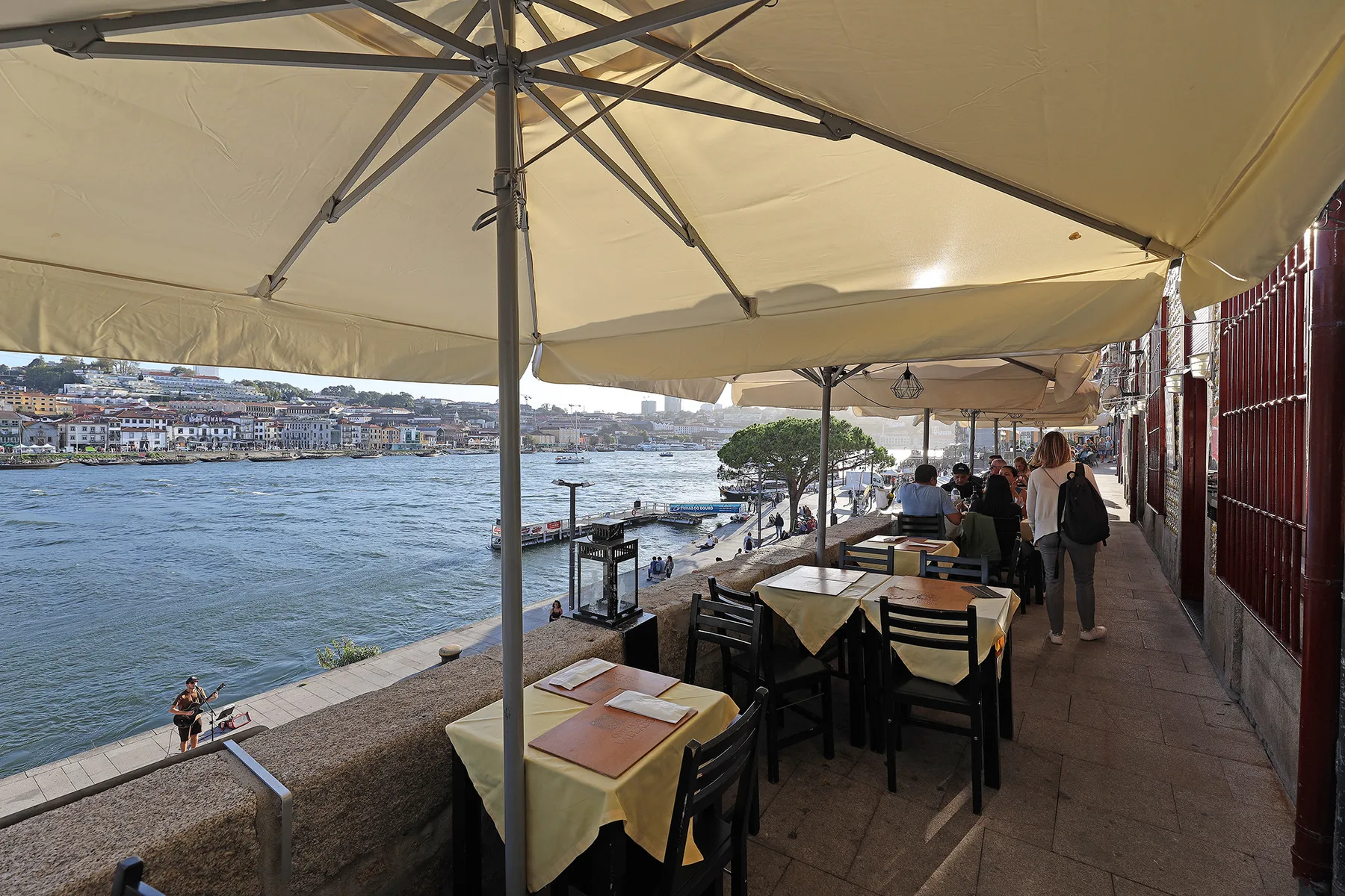 A riverside dining terrace with tables under large umbrellas.