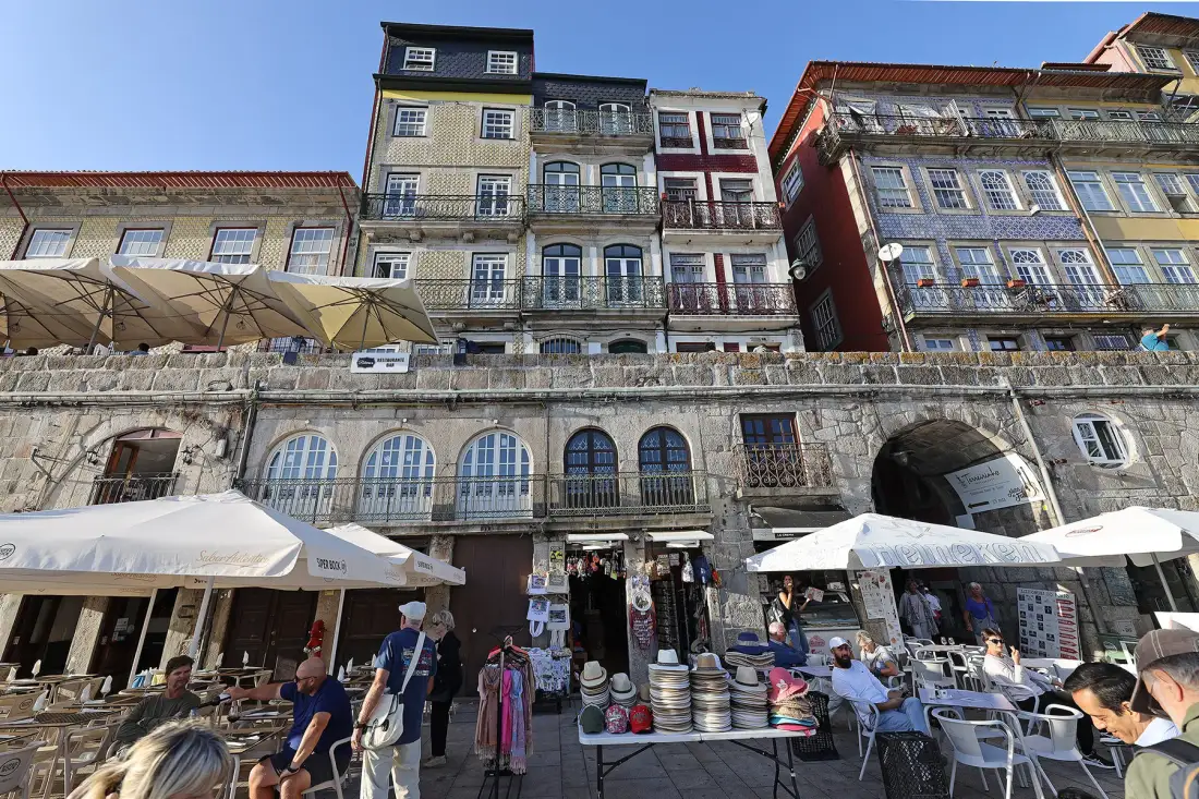 A waterfront street scene with historic buildings, outdoor café seating, and market stalls.