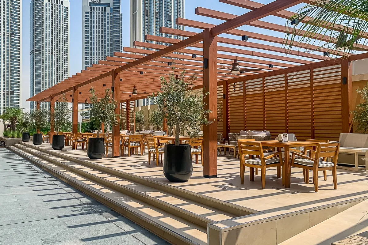 Una terraza exterior con mesas y asientos bajo una pérgola de madera.