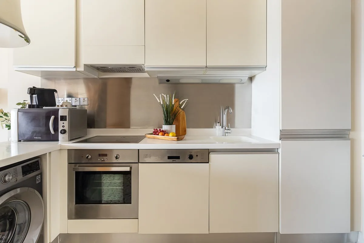Una cocina moderna con armarios claros, un horno integrado y una lavadora.