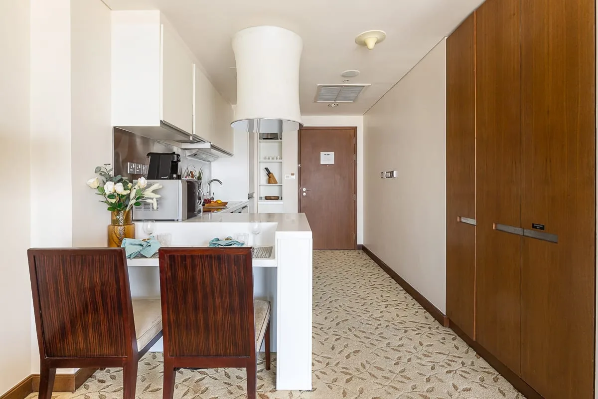 Una pequeña cocina y zona de comedor da a un pasillo con una puerta marrón.