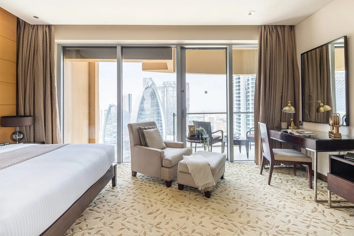 Un dormitorio luminoso con una zona de estar junto a ventanas amplias con vistas a edificios de la ciudad.