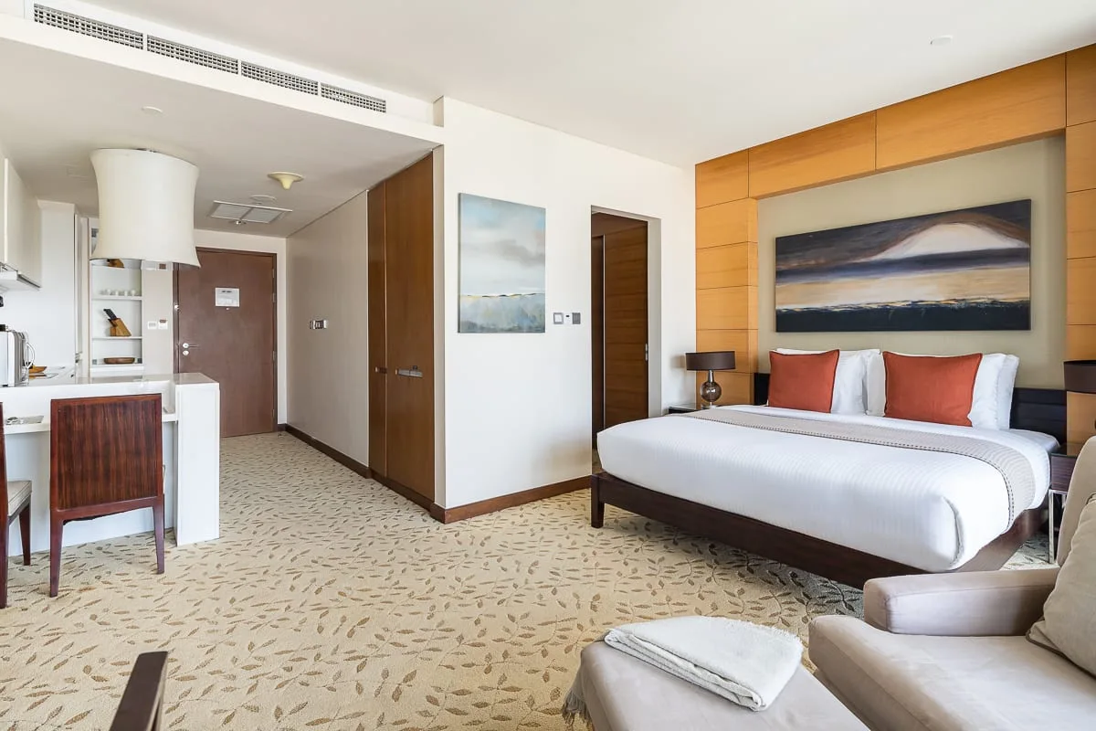 Un dormitorio de hotel con una cama grande, asientos junto a la cama y una pequeña cocina.