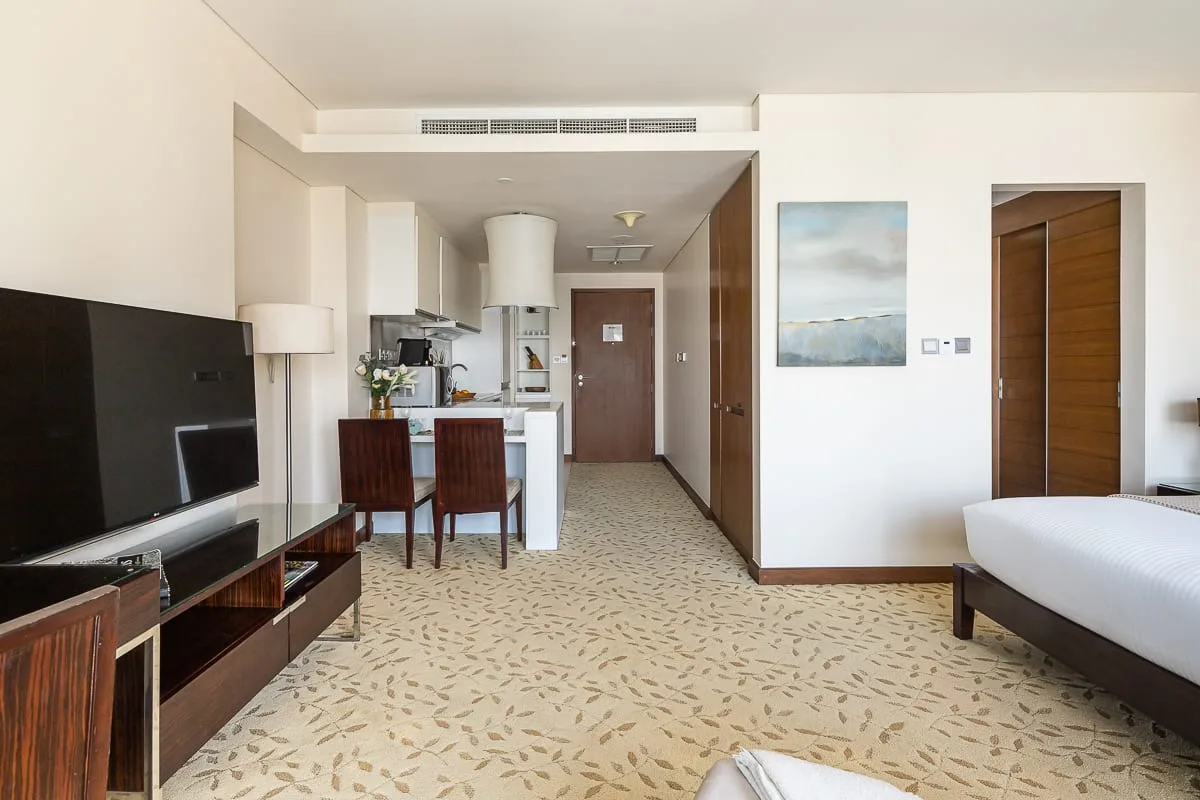 Una habitación luminosa con cocina pequeña, barra de comedor, televisor y cama.