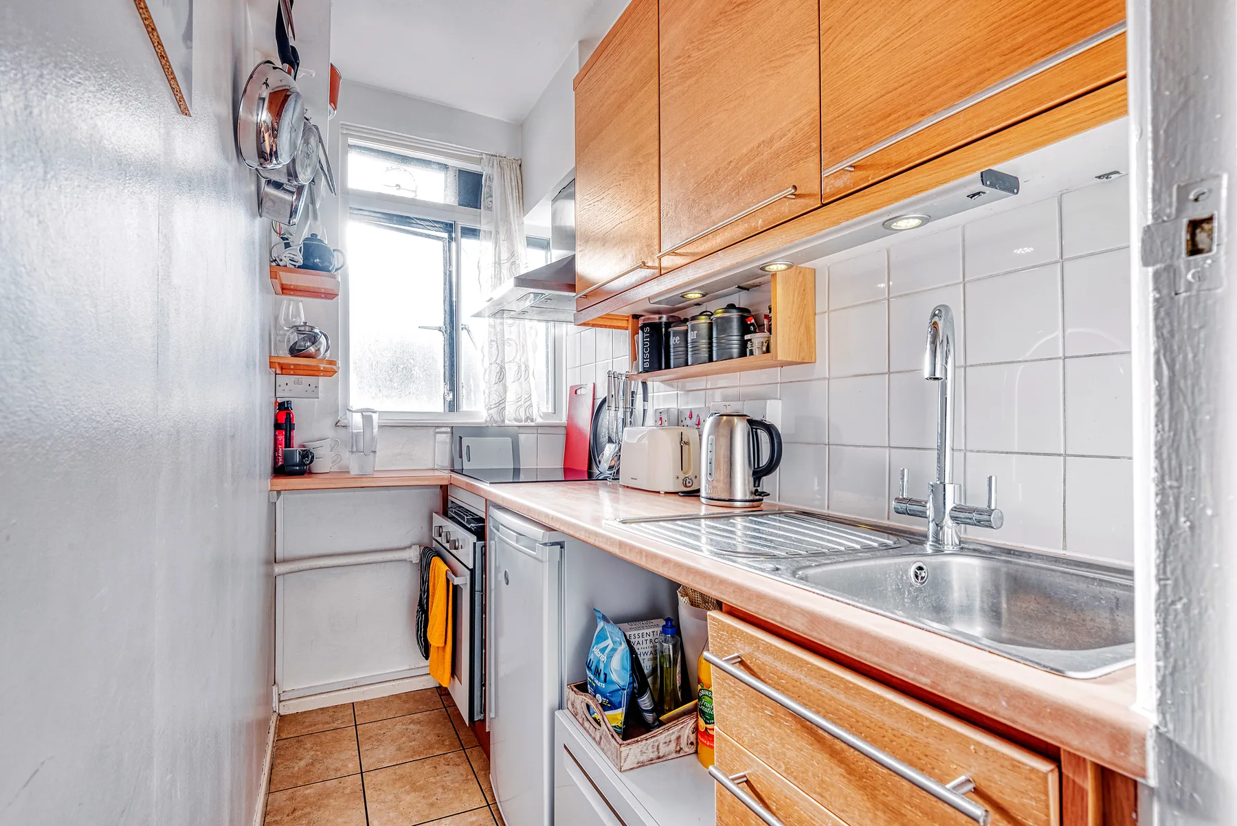 Una cocina compacta con gabinetes de madera, una encimera y un fregadero de acero inoxidable.