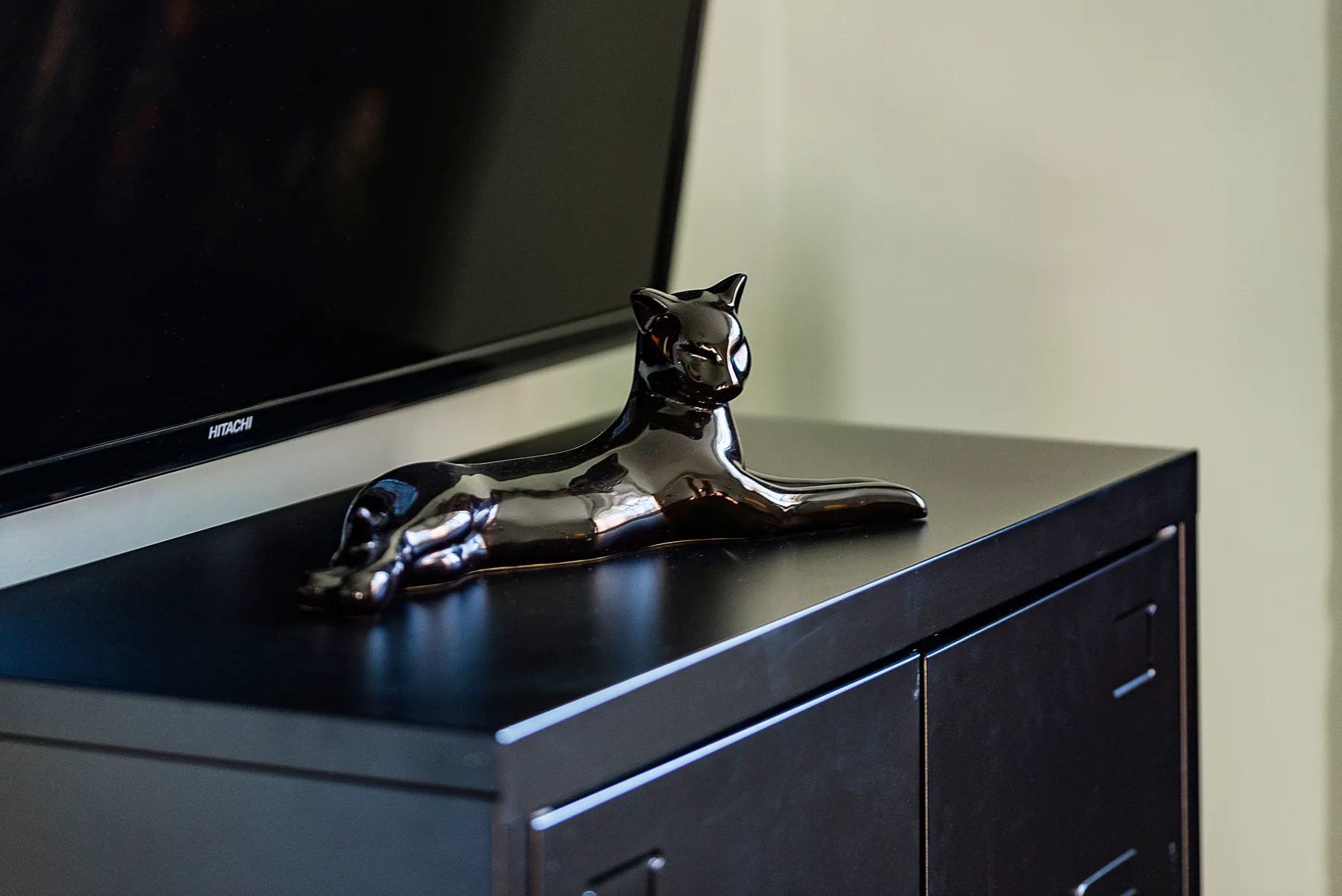 Un televisor está sobre un mueble oscuro, con una figura brillante de gato encima.