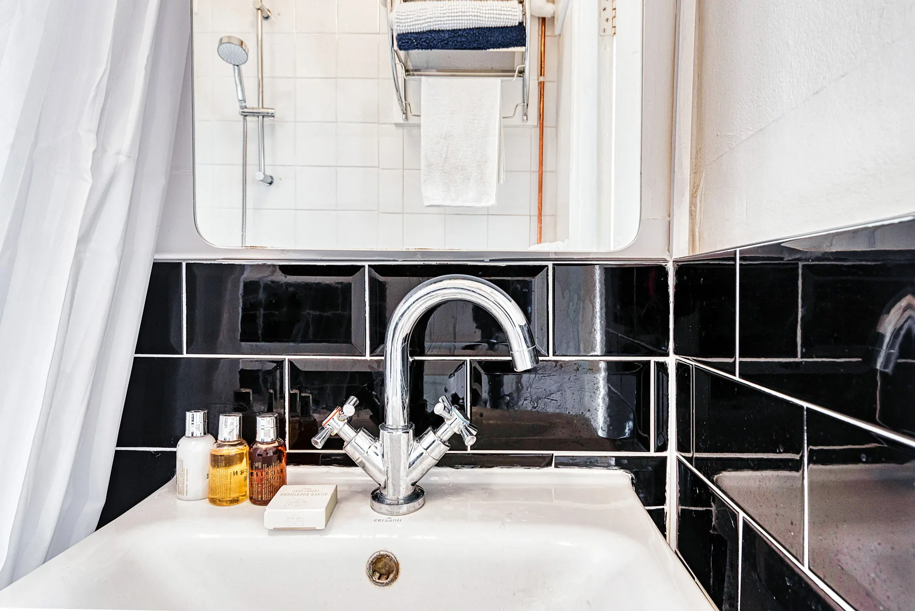 Un lavabo de baño está bajo un espejo, con azulejos negros en las paredes.