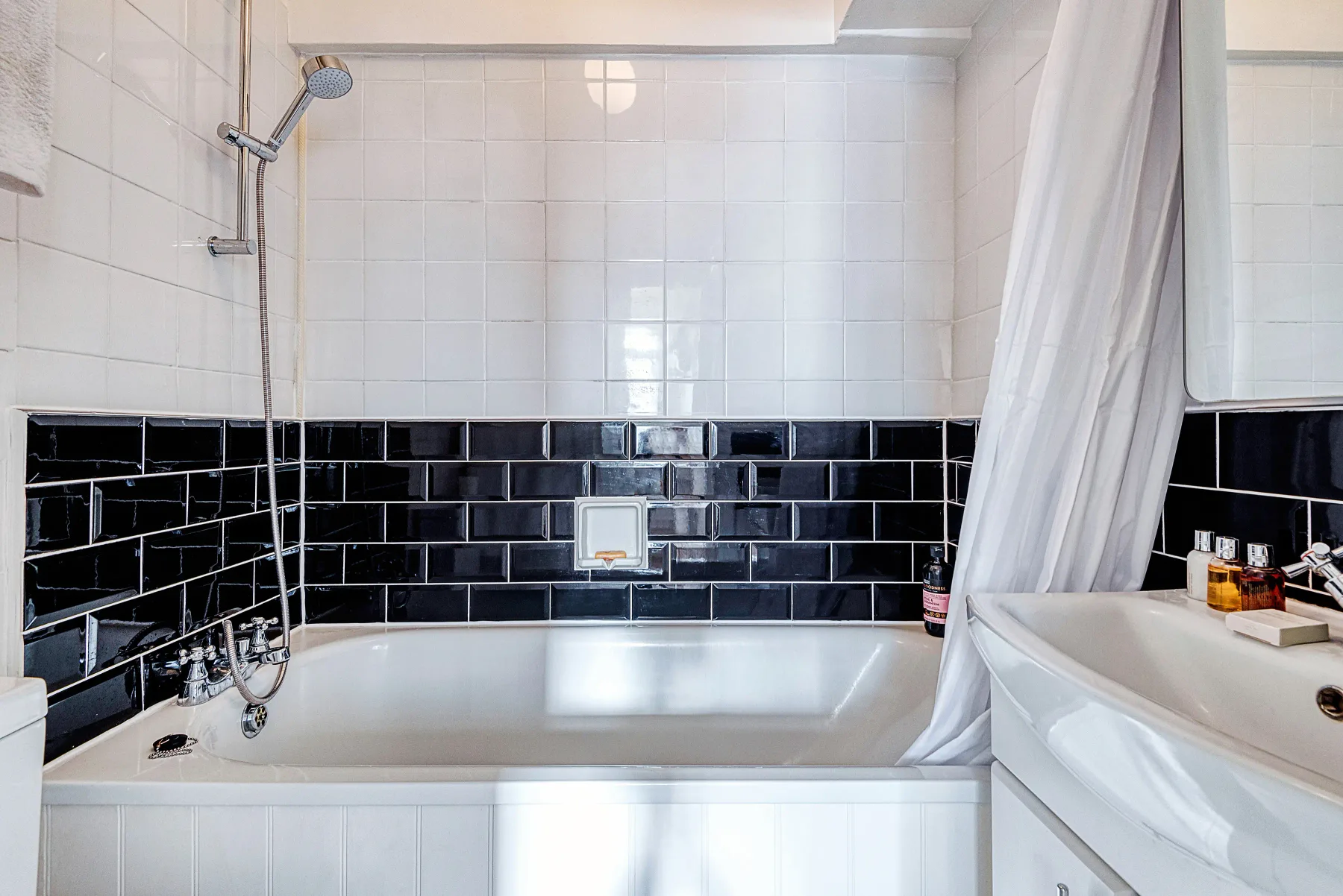 Un baño con bañera, ducha y paredes de azulejos blancos.