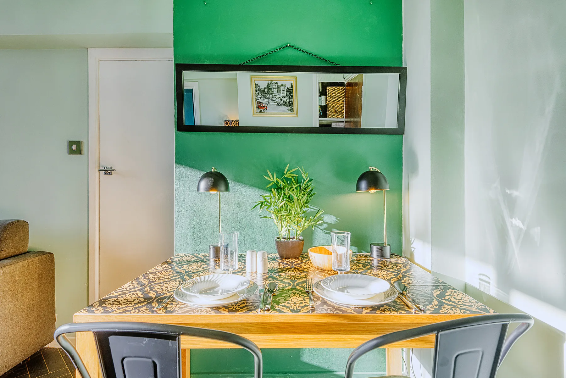 Comedor con una mesa puesta, una pared verde y dos lámparas.