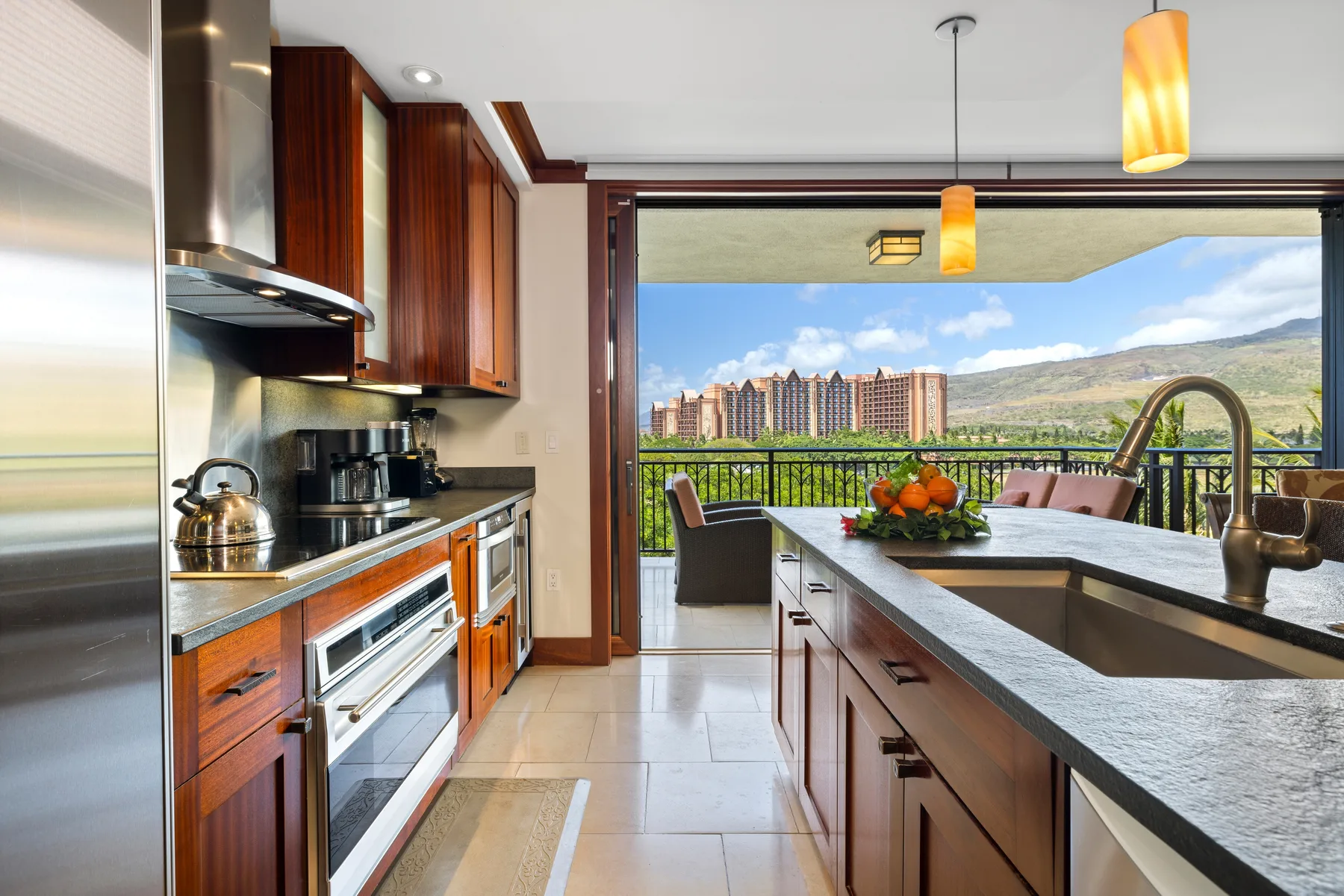 Una cocina moderna se abre a un balcón con vistas a colinas y edificios.