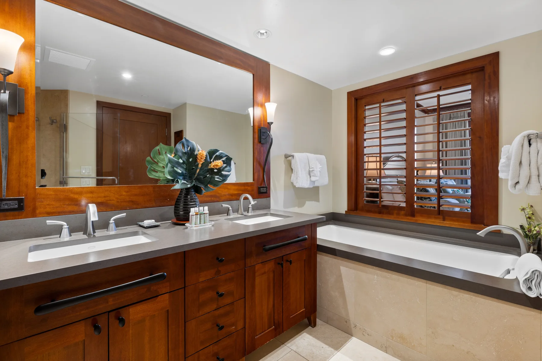 Un tocador de baño con un espejo amplio y una ventana con persianas de madera.