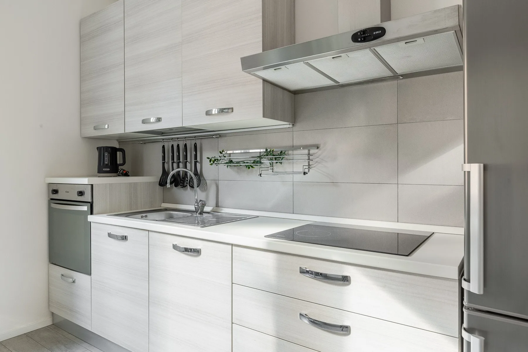 A modern kitchen with white cabinetry, a sink, and a cooktop.