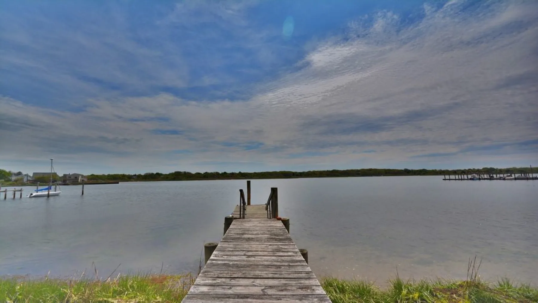 Un muelle de madera se extiende sobre aguas tranquilas bajo un cielo nublado.