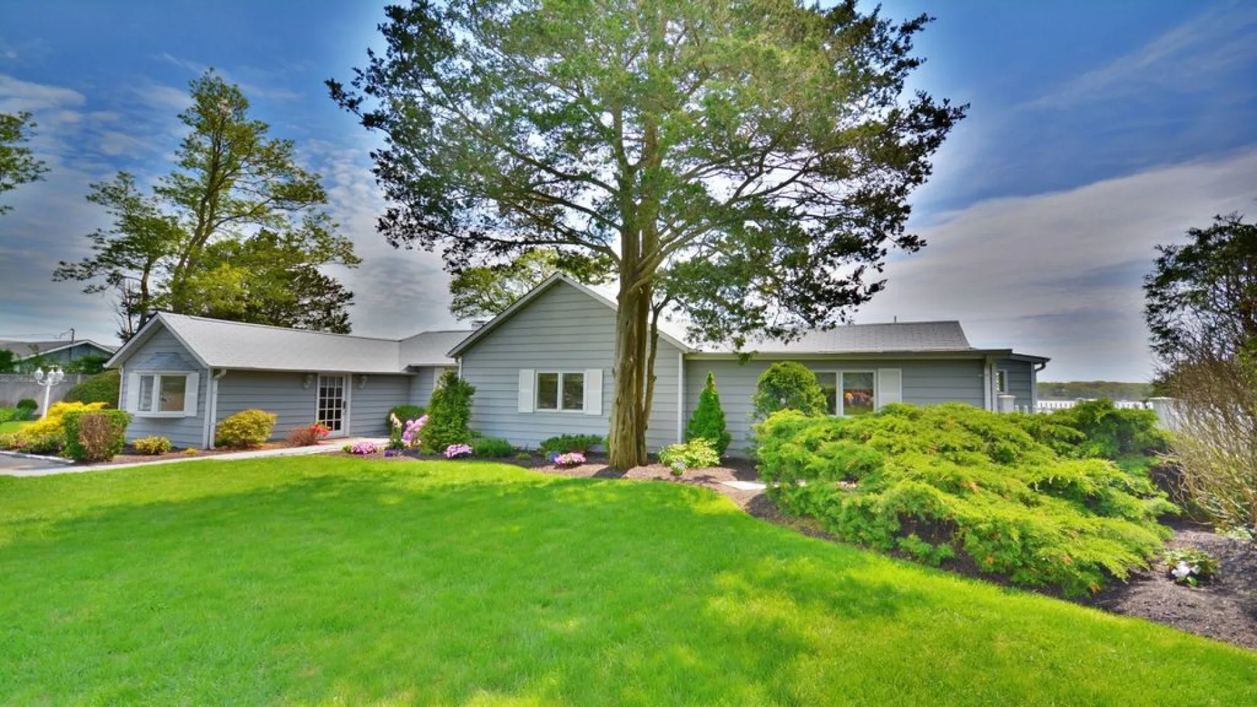 A single-story house stands behind a green lawn and landscaped shrubs.