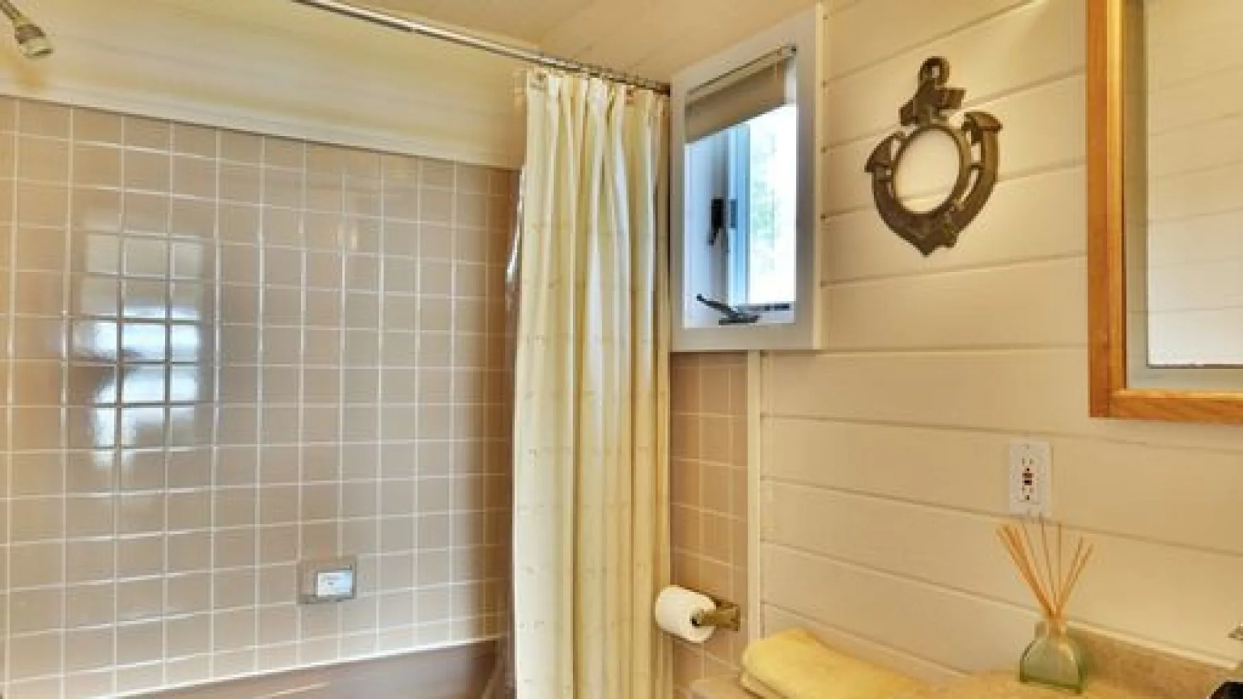 Un baño con una zona de ducha alicatada y una ventana con cortina.