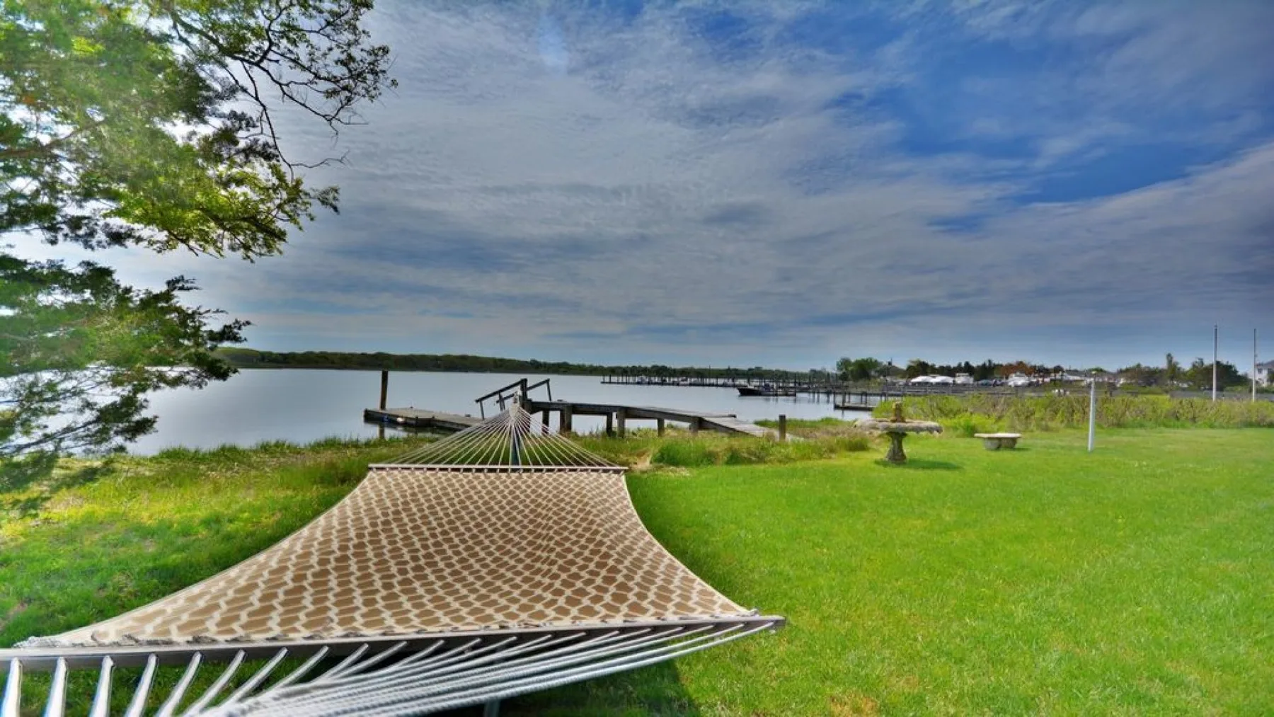 A hammock rests on a grassy lakeshore beside a wooden dock.