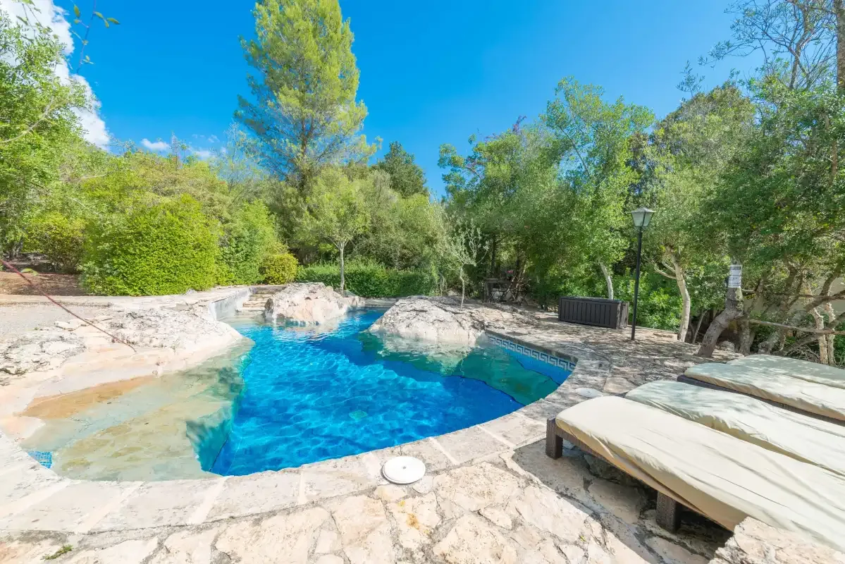 Una piscina al aire libre rodeada de árboles, con una tumbona acolchada al lado.