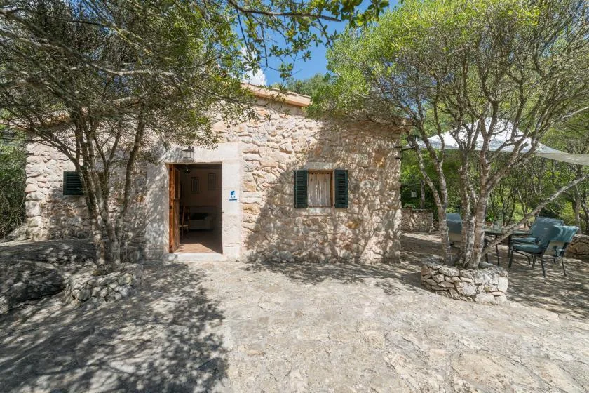 Un edificio de piedra con la puerta abierta está entre árboles, junto a una zona de estar al aire libre.