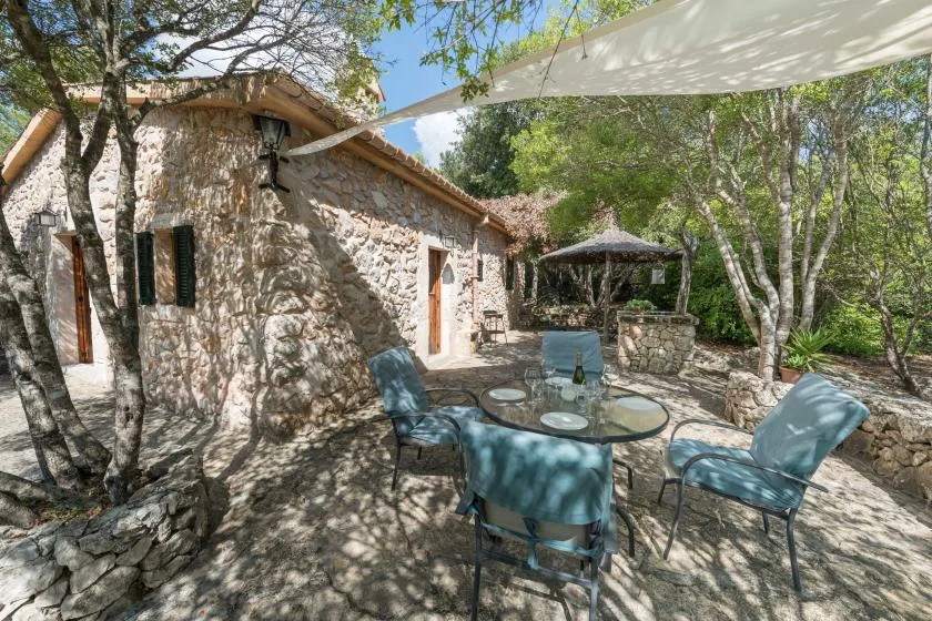 Una casa de piedra da a un patio sombreado con asientos y una mesa al aire libre.