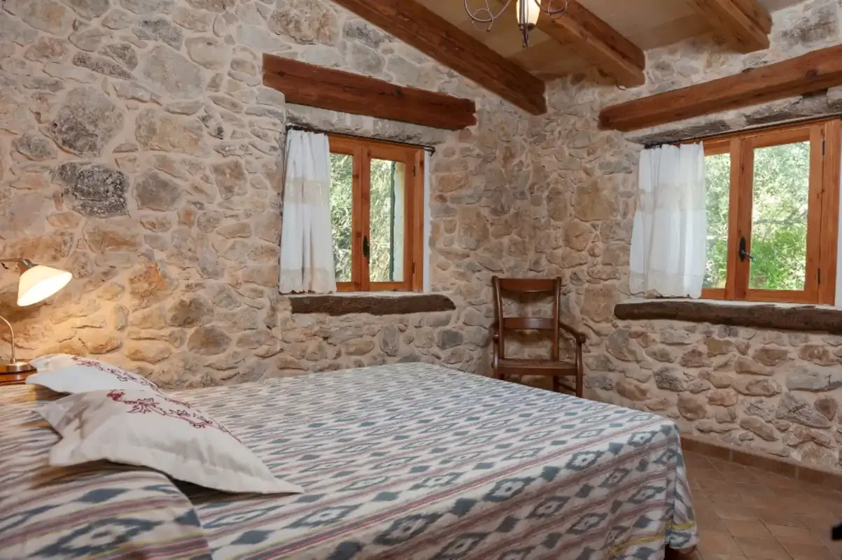 Un dormitorio con ropa de cama estampada, paredes de piedra vista y vigas de madera.