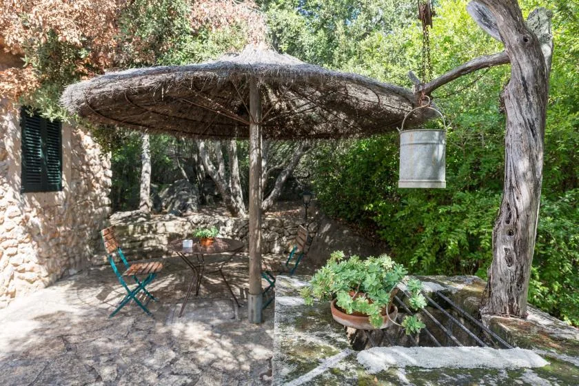 Un patio de piedra sombreado con una cubierta rústica, asientos y plantas en macetas.