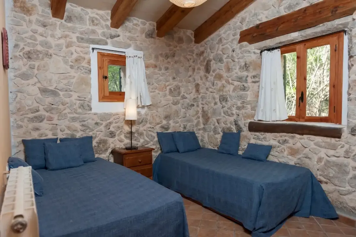 Un dormitorio de paredes de piedra con camas cubiertas de azul y vigas de madera.