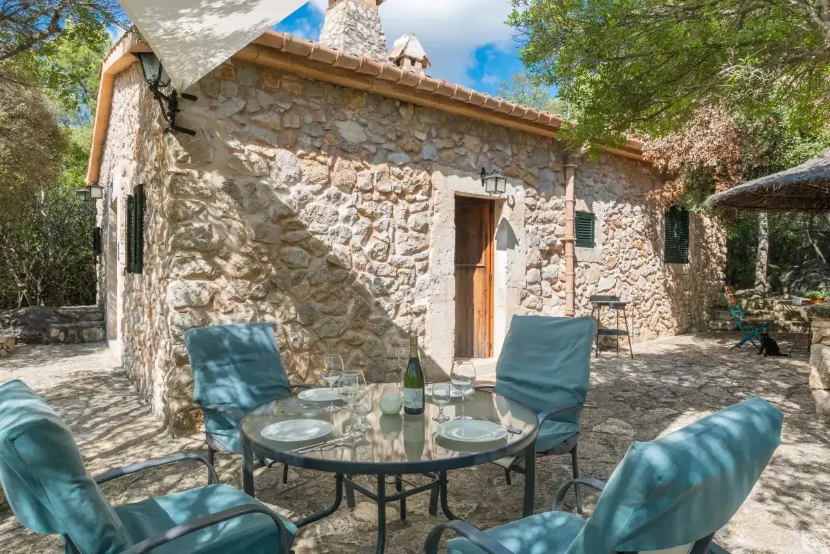Una casa de piedra da a un patio pavimentado con asientos al aire libre y una mesa de vidrio.