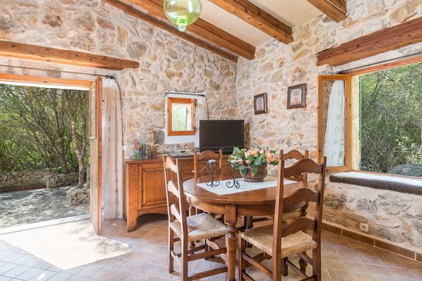 Un comedor rústico con una mesa y sillas de madera junto a grandes ventanas.