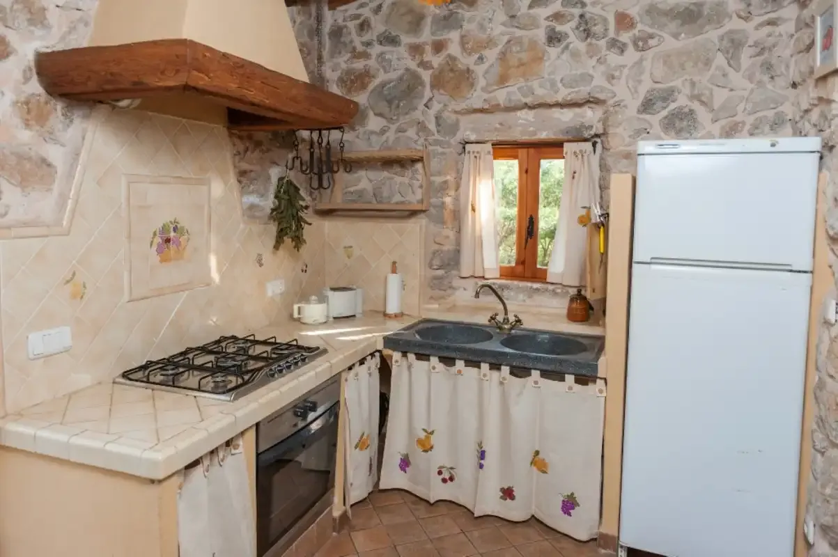 Una cocina rústica con paredes de piedra, una encimera de azulejos y una ventana.