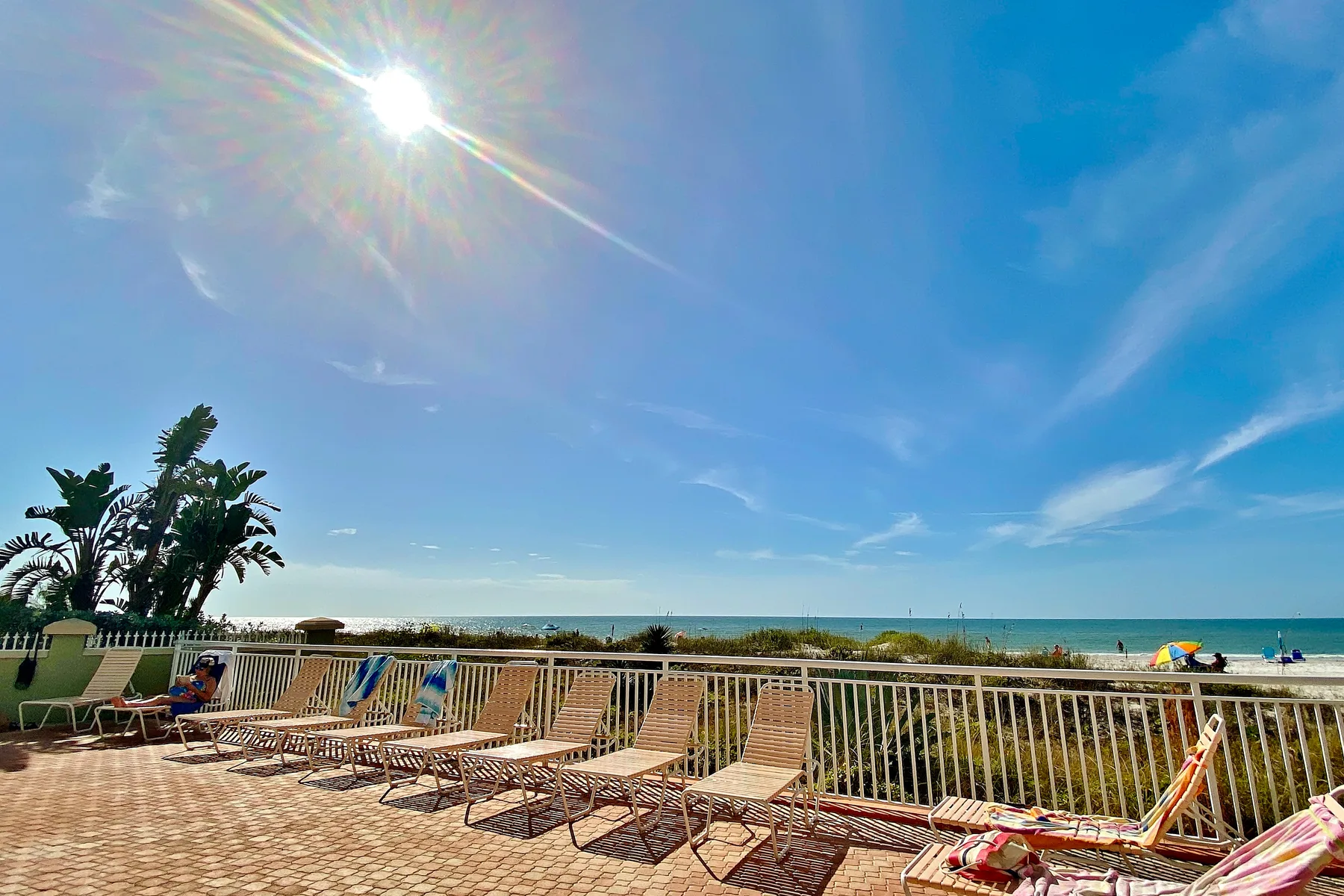 A sunny seaside terrace has rows of lounge chairs facing the ocean.
