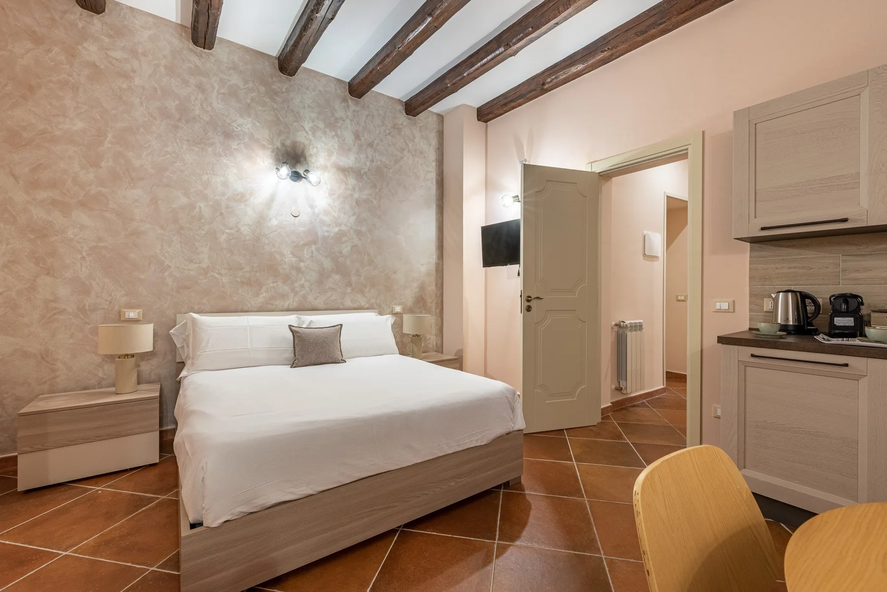Un dormitorio con una cama bien tendida y vigas expuestas en el techo.