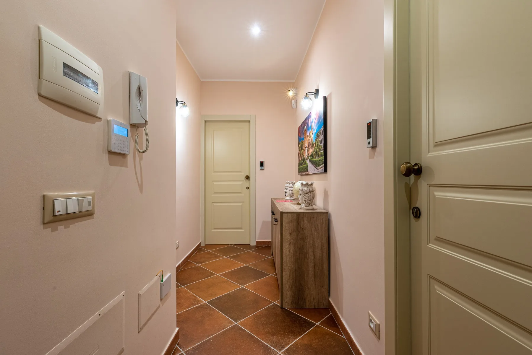 Un pasillo estrecho con suelo de baldosas, una puerta cerrada y un pequeño mueble.