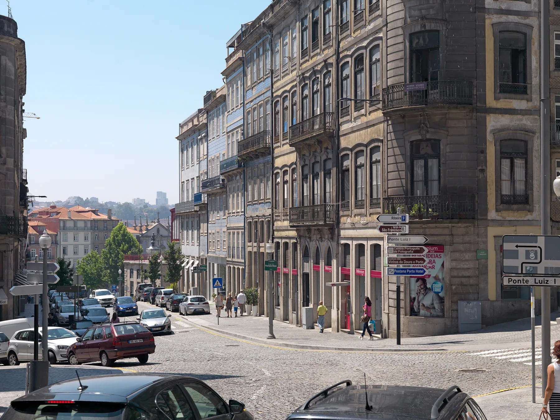 A city street lined with tall historic buildings and parked cars.