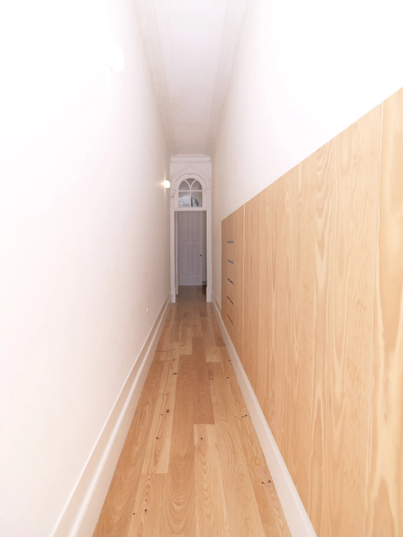 A narrow hallway with wood flooring leads to a door at the far end.