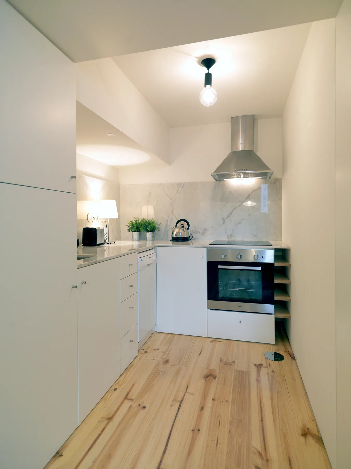 A compact kitchen with white cabinets, a cooktop, and a wood-toned floor.
