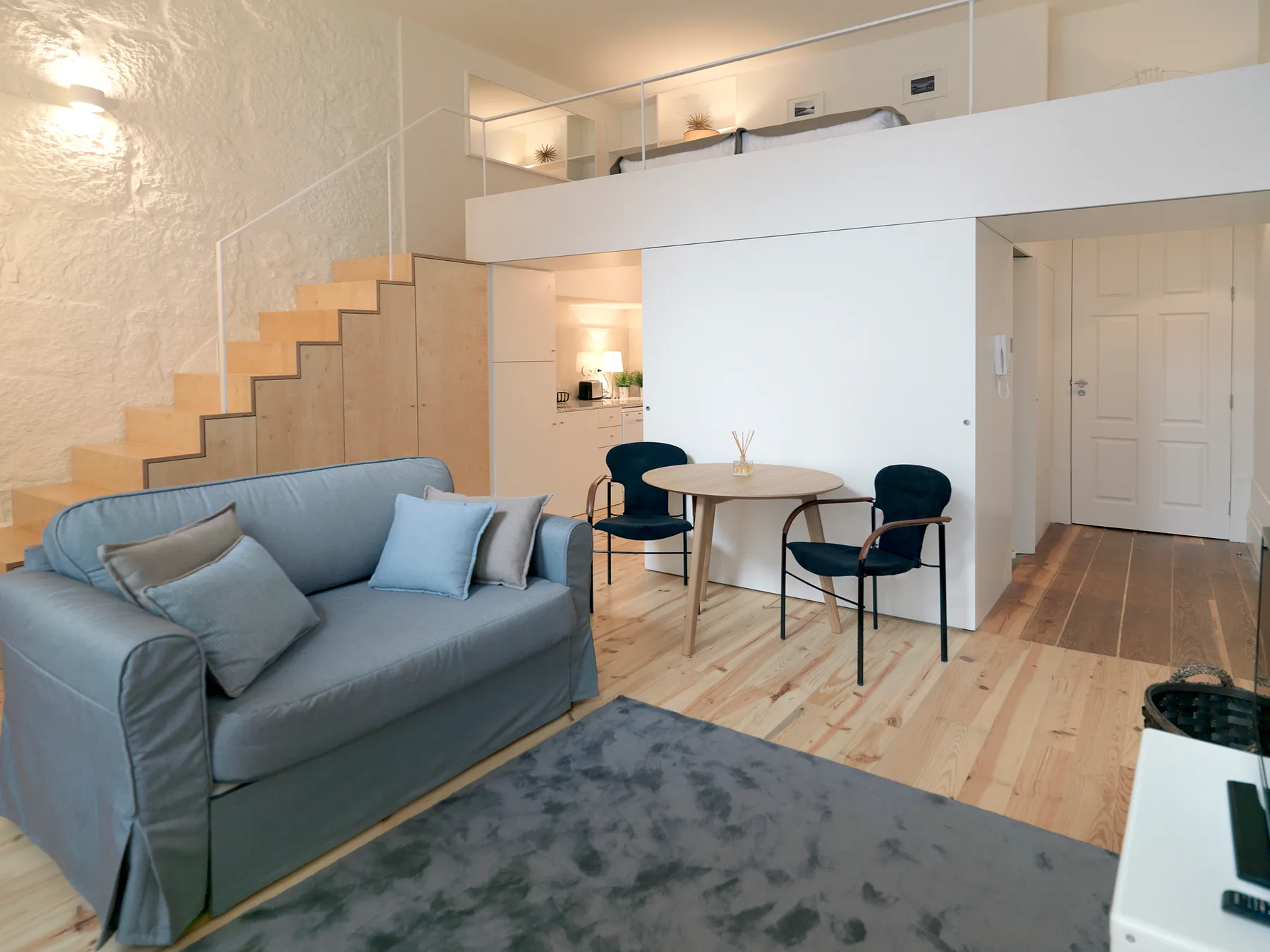 A modern living area with seating, a small dining table, and stairs to a loft.