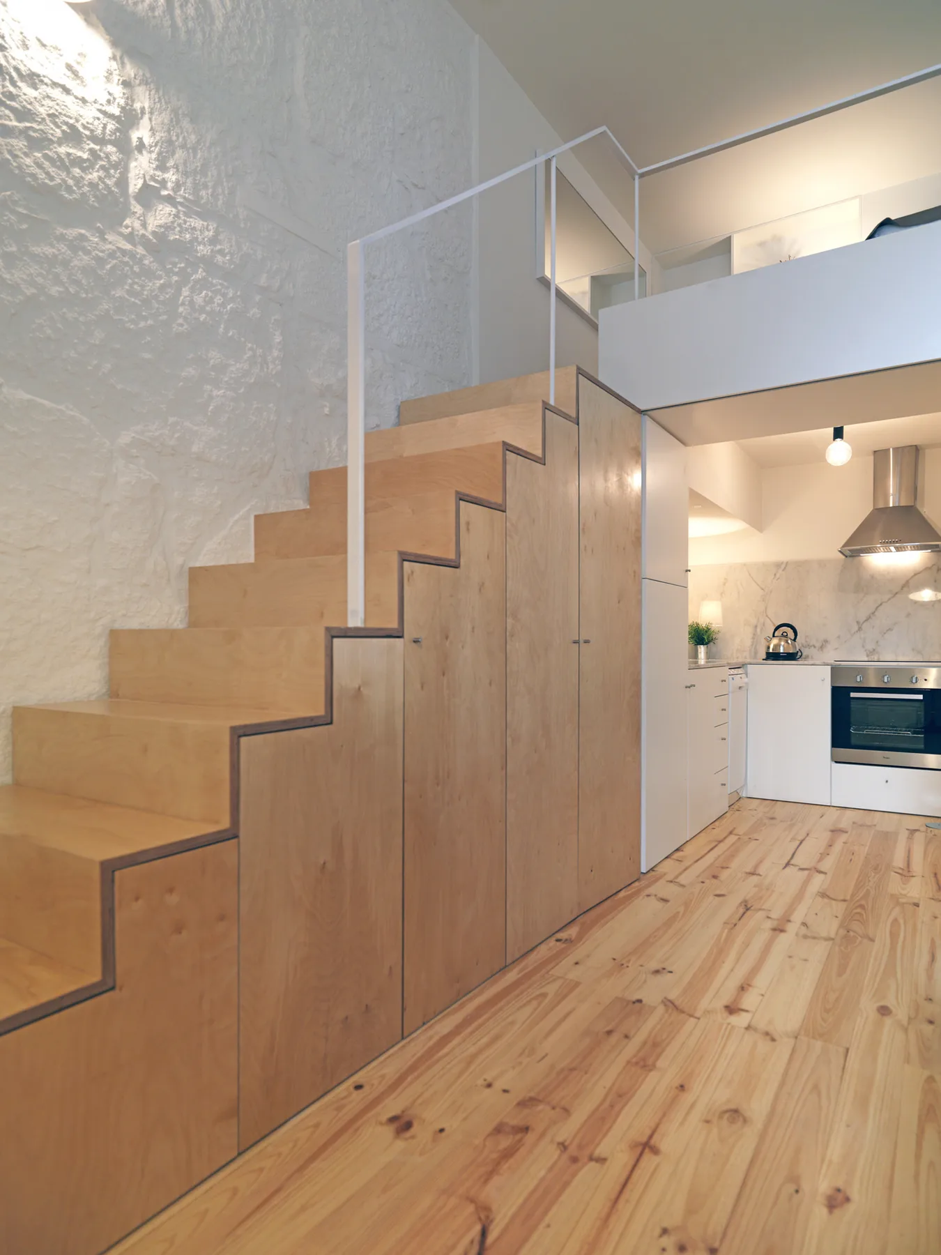 A compact kitchen sits beside a wooden staircase with built-in storage.
