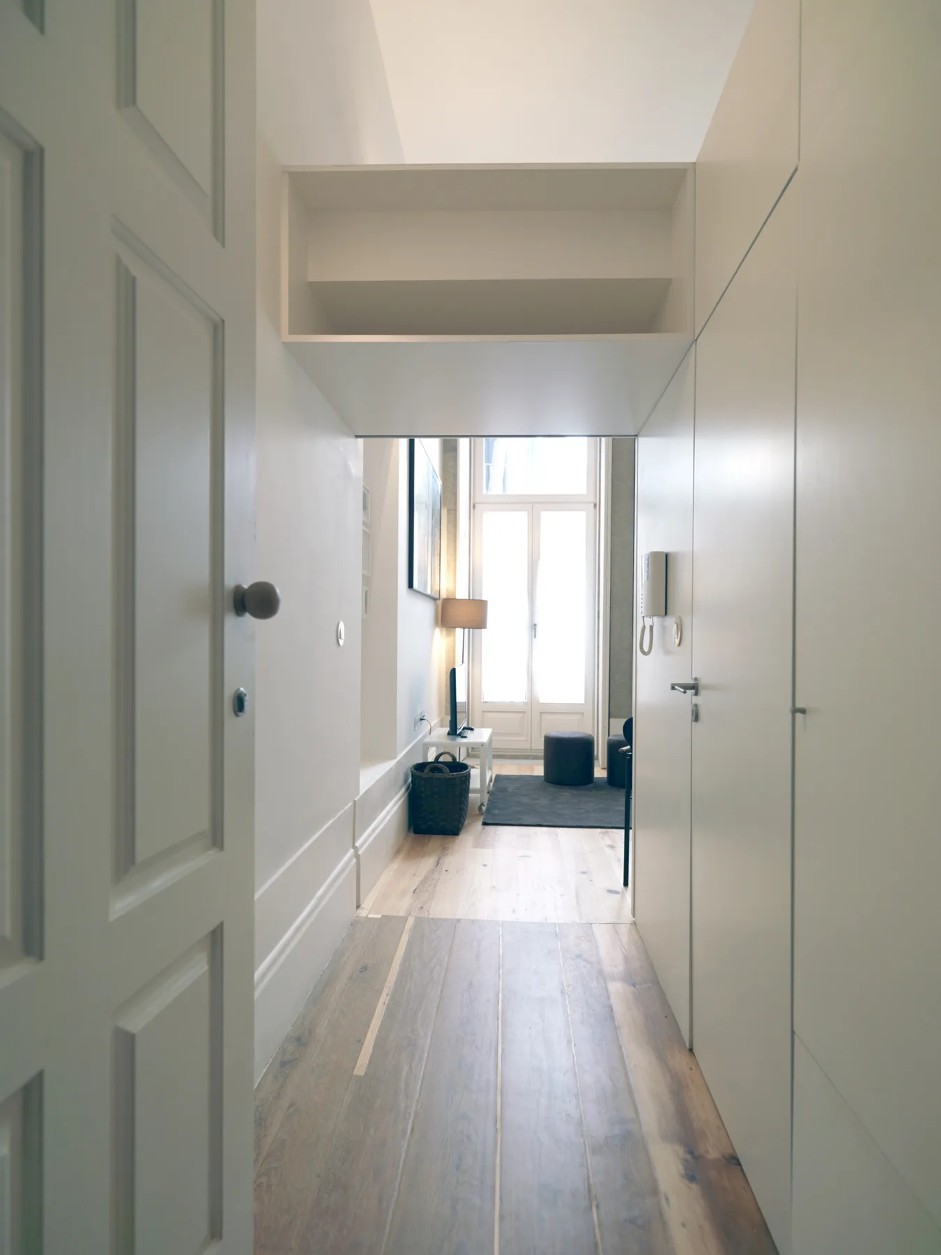 A bright apartment hallway leads to a window and a small seating area.