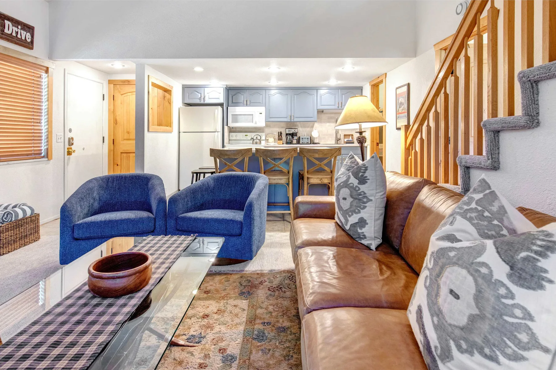 A living room with blue seating, a brown couch, and a kitchen in the background.