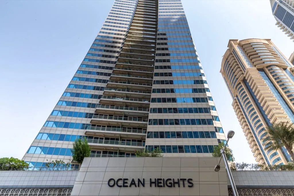 Un edificio alto moderno con ventanas azules se alza sobre un letrero que dice Ocean Heights.