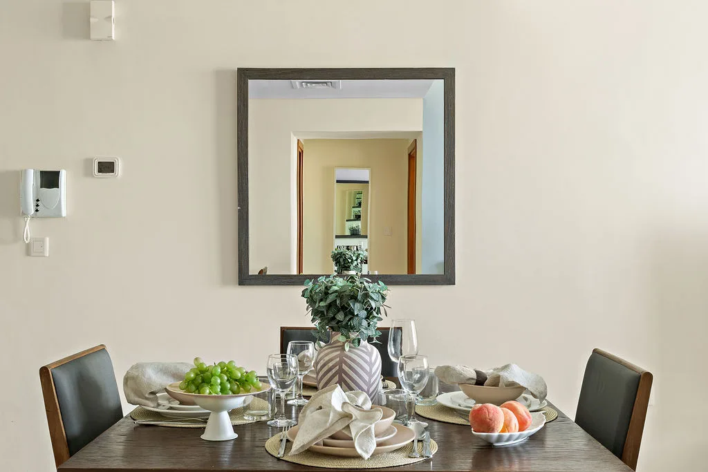 Una mesa de comedor está puesta con platos, copas, fruta y un centro de mesa con hojas.