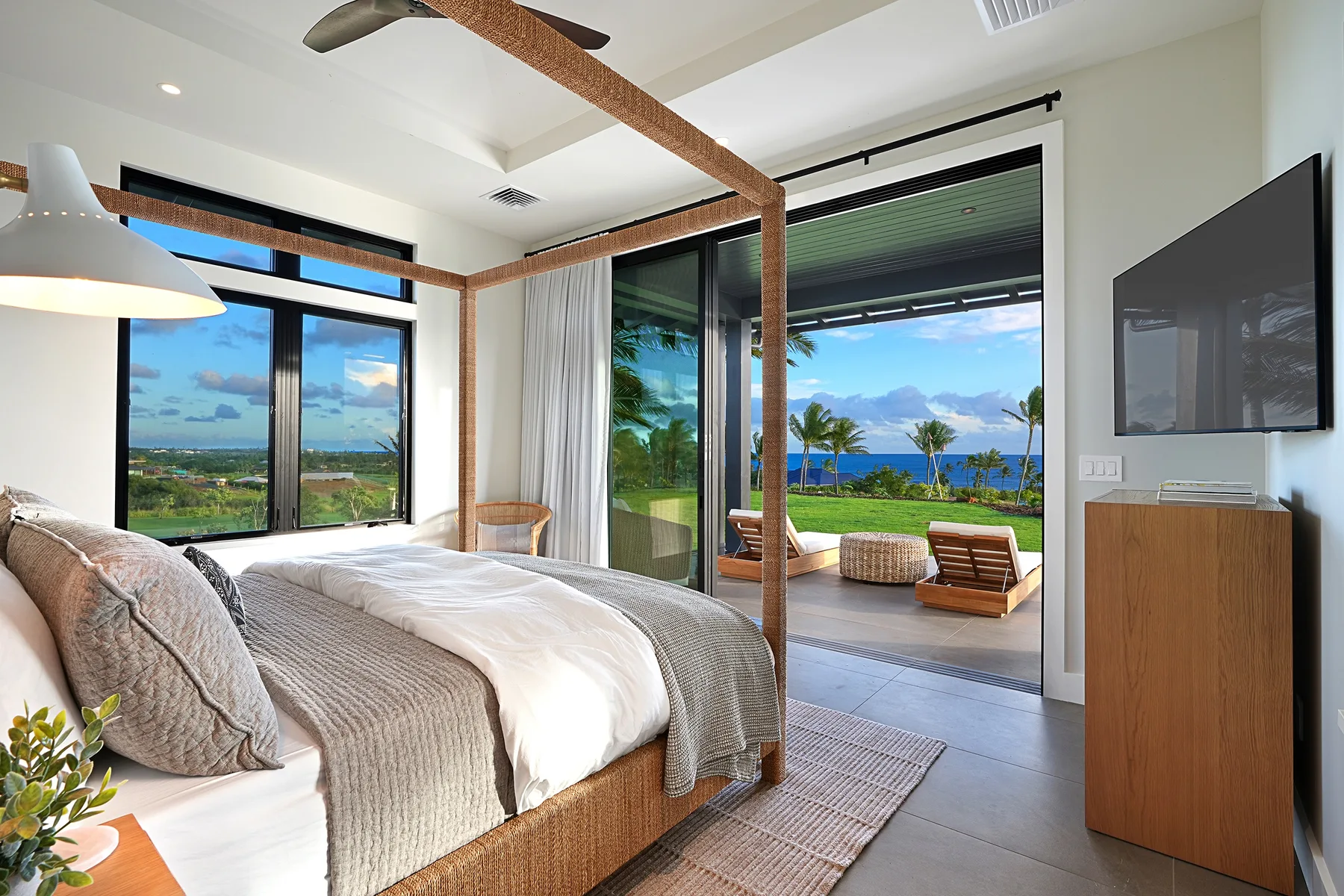 A bedroom opens onto a covered patio with views of the ocean and palm trees.
